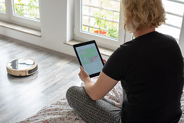 Image showing Woman is steering her vacuum cleaning robot from the bed