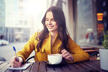 Image showing happy woman with notebook drinking cocoa at cafe