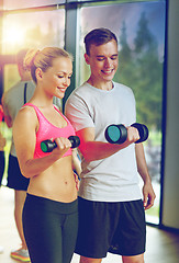 Image showing smiling young woman with personal trainer in gym