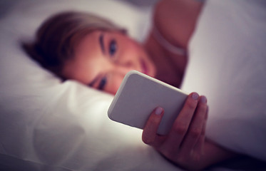 Image showing young woman with smartphone in bed at home bedroom