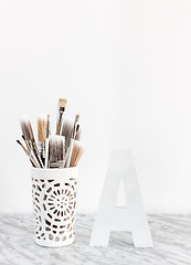 Image showing Paintbrushes in a decorative vase and letter A on marble surface