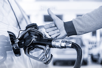 Image showing Petrol or gasoline being pumped into a motor vehicle car. Closeup of man, showing thumb up gesture, pumping gasoline fuel in car at gas station.