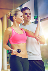 Image showing smiling young woman with personal trainer in gym