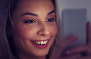 Image showing happy smiling young woman with smartphone at night