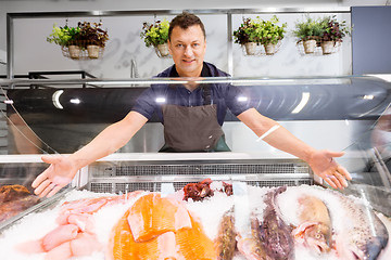 Image showing male seller showing seafood at fish shop fridge