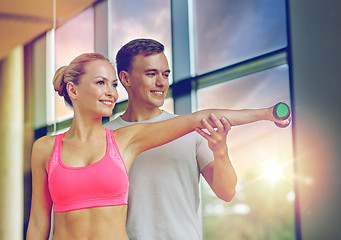 Image showing smiling young woman with personal trainer in gym