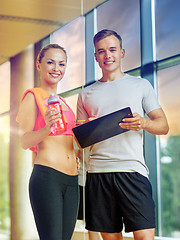 Image showing smiling young woman with personal trainer in gym