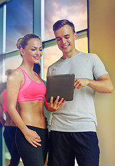 Image showing smiling young woman with personal trainer in gym