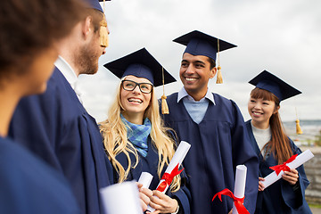 Image showing happy students in mortar boards with diplomas