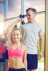 Image showing smiling young woman with personal trainer in gym