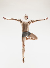 Image showing Athletic ballet dancer in a perfect shape performing over the grey background.
