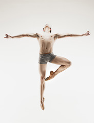 Image showing Athletic ballet dancer in a perfect shape performing over the grey background.