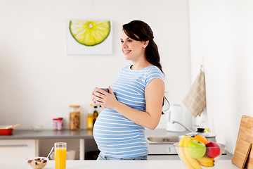 Image showing happy pregnant woman with cup at home kitchen