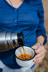 Image showing Woman pouring hot tea from a thermos on a sandy beach on a Sunny day. Close up.