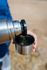 Image showing Woman pouring hot tea from a thermos on a sandy beach on a Sunny day. Close up.