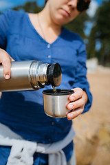 Image showing Woman pouring hot tea from a thermos on a sandy beach on a Sunny day. Close up.