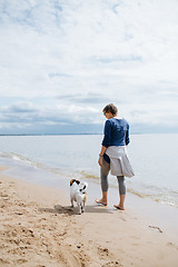 Image showing Woman walking with her dog on the sandy beach. Rear view.