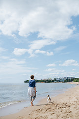 Image showing Woman walking with her dog on the sandy beach. Rear view.