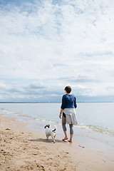 Image showing Woman walking with her dog on the sandy beach. Rear view.