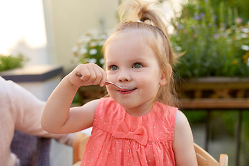 Image showing happy little girl with spoon eating outdoors