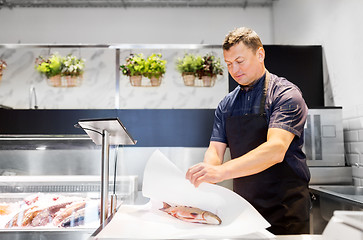 Image showing seller wrapping fish into paper at seafood shop