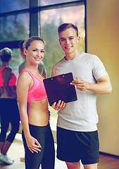 Image showing smiling young woman with personal trainer in gym