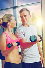 Image showing smiling young woman with personal trainer in gym