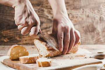 Image showing Whole grain bread put on kitchen wood plate with a chef holding gold knife for cut.