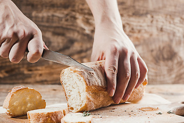 Image showing Whole grain bread put on kitchen wood plate with a chef holding gold knife for cut.