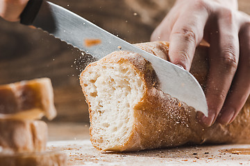 Image showing Whole grain bread put on kitchen wood plate with a chef holding gold knife for cut.