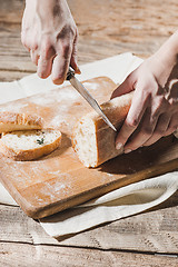 Image showing Whole grain bread put on kitchen wood plate with a chef holding gold knife for cut.