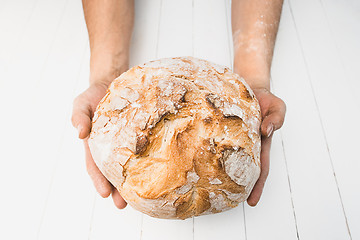 Image showing Closeup of male hands put fresh bread on an old rustic table on black background with copy space for your text