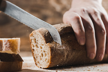 Image showing Whole grain bread put on kitchen wood plate with a chef holding gold knife for cut.