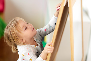 Image showing happy little girl drawing on chalk board at home