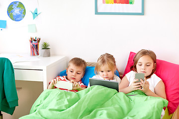 Image showing kids with tablet pc and smartphones in bed at home