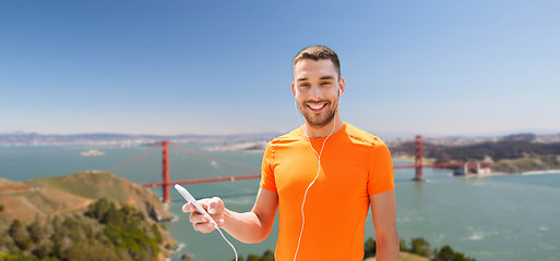 Image showing man with smartphone and earphones over golden gate