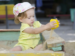 Image showing A girl is pouring sand in a sandbox