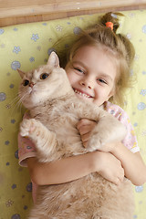 Image showing Little girl hugging a cat lying on a mattress on the floor