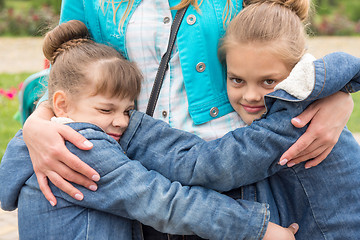 Image showing Two girls hug mother tightly