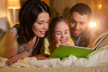 Image showing happy family reading book in bed at night at home