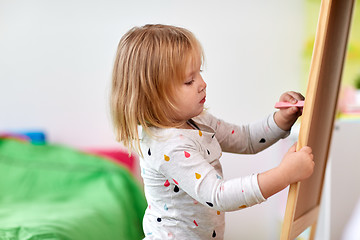 Image showing happy little girl drawing on chalk board at home