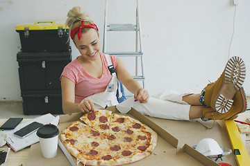 Image showing Woman in overalls eating pizza at workplace 