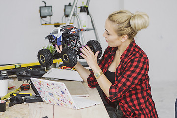 Image showing Young woman inspecting radio-controlled car at workbench 