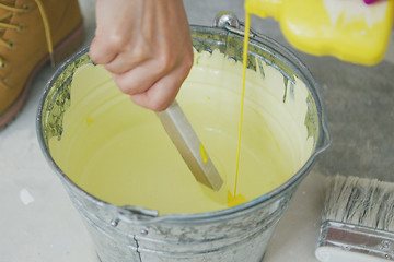 Image showing Hand mixing yellow wall paint in bucket 