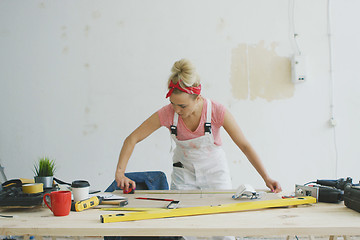 Image showing Female carpenter measuring wood on workbench 