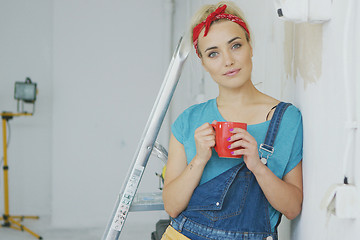 Image showing Smiling female in overalls leaning on wall 