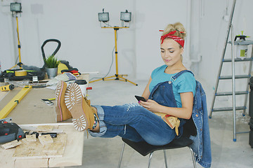 Image showing Woman resting with smartphone at carpenter workbench 