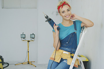 Image showing Happy woman with drill sitting on stepladder 