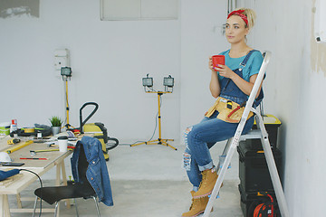 Image showing Female carpenter resting on stepladder with beverage 