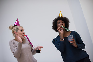 Image showing smiling women in party caps blowing to whistles